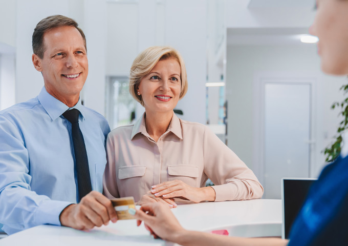 Dr. Peter J. Kim and a masked dental assistant at Pecan Tree Family Dentistry in McKinney, TX, perform a same-day dental procedure on a reclining patient, with digital X-rays displayed on a monitor behind them.